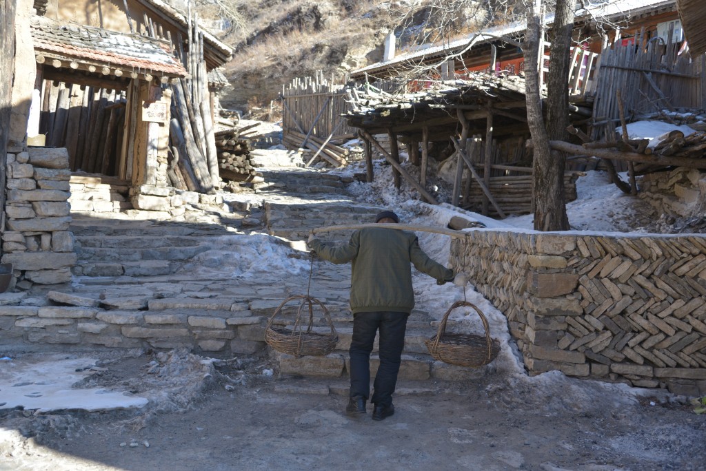 时值严冬,村子周围到处都是白雪,一名村民提着担子,准备铲雪。