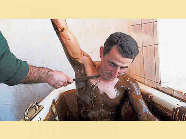 泡黑油澡时，有服务人员在旁，帮忙刮除黏在身上的原油。
