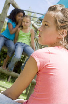 Two young girl friends at a playground whispering about other gi