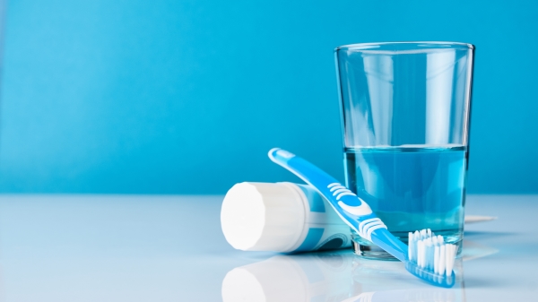 A blue toothbrush with toothpaste and glass of blue mouthwash on blue background with copy space, close-up. Dental oral hygiene concept