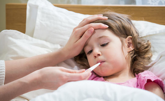 Mother measuring temperature of her ill kid. Sick child with high fever laying in bed and mother holding thermometer. Hand on forehead.