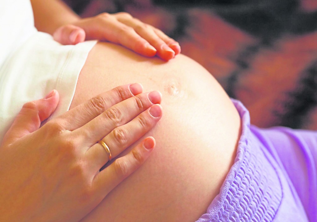 Young pregnant woman holding and touching her belly, closeup