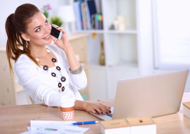 Young businesswoman sitting at the desk and talking on phone
