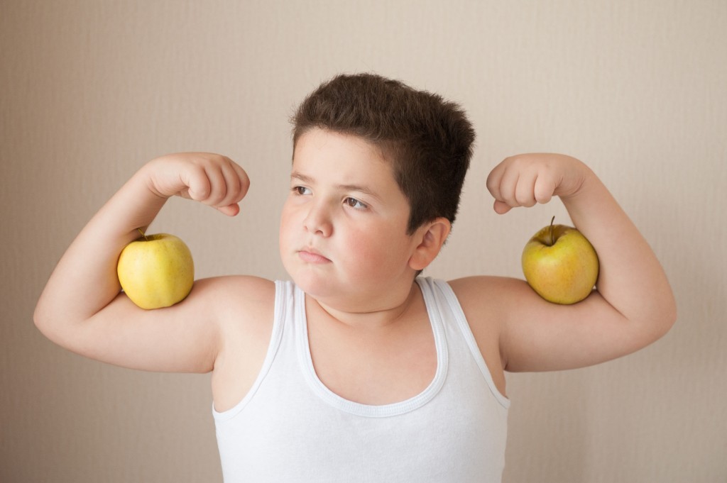 fat boy in t-shirt shows muscles with apples on his biceps