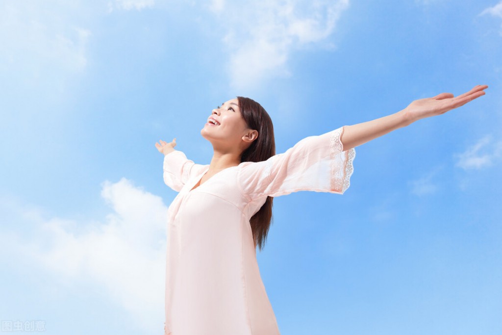Beautiful woman breathing fresh air with raised arms with a cloudy blue sky in the background