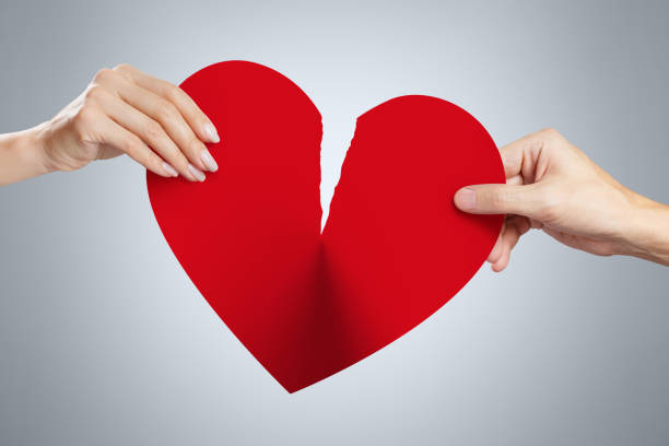 Male and female hands tearing a red heart symbol of love in half