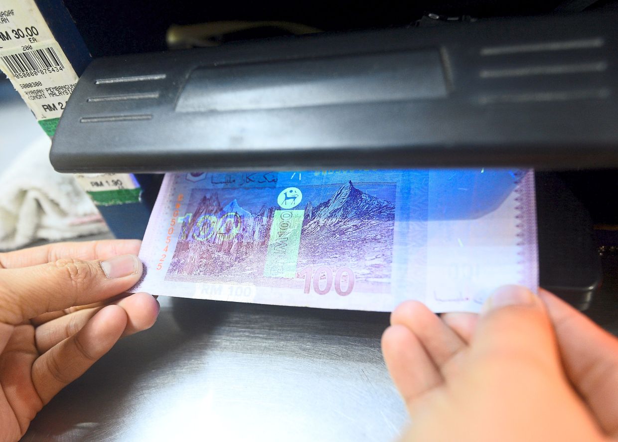 A cashier using Ultraviolet lights machines for detecting fake money at a mall in Subang Jaya. (30/9/2022). —AZHAR MAHFOF/The Star