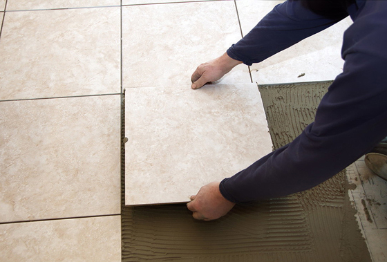 A man on his knees installing a ceramic tile floor